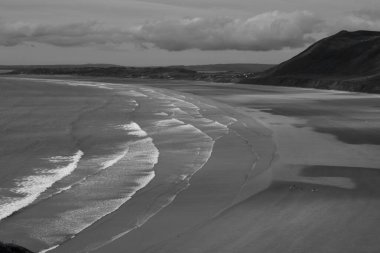 Gower Yarımadası 'ndaki Worm' s Head 'deki uçurum yüzeyi altın kum ve dalgaların aktığı Llangennith' teki muhteşem sahili incelemek için mükemmel bir görüş açısı sunuyor. İnsanlar manzaranın tadını çıkarıyor