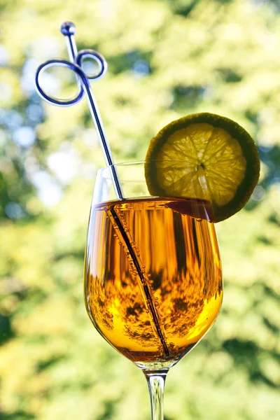 Orange fizzy drink with a slice of lemon, straw in a wine glass against green background