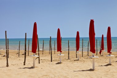 Kırmızı kapalı şemsiye ve ahşap direklerin bir kum plajındaki Akdeniz, Sicilya, güneşli yaz gününde