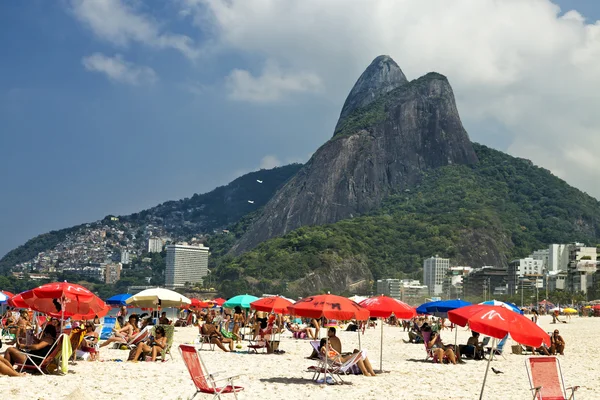As pessoas estão tomando banho de sol, relaxando, sob guarda-sóis de praia na praia de Ipanema, no Rio de Janeiro, em um dia quente e ensolarado. — Fotografia de Stock