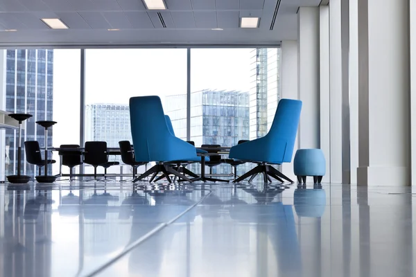 Krzesła nowoczesne biuro wirowały niebieski w przewiewne otworzyć pokój z dużymi oknami i niewyraźne budynków poza. — Zdjęcie stockowe