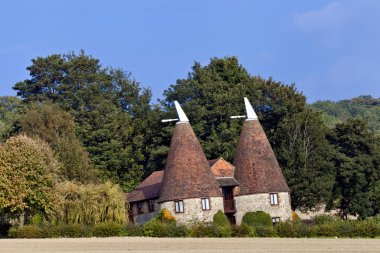 Old traditional Kentish round stone oast house with white tipped cowls, red tiled roof in south east English countryside, used for drying hops. clipart