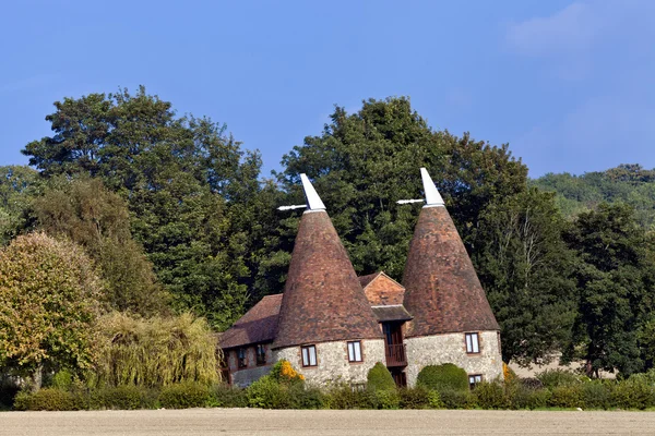 Old traditional Kentish round stone oast house with white tipped cowls, red tiled roof in south East English countryside, used for drying hops . — стоковое фото