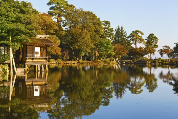 Casa de té tradicional japonesa antigua en alambiques en el jardín con árboles en colores otoñales, y reflejos en el agua — Foto de Stock