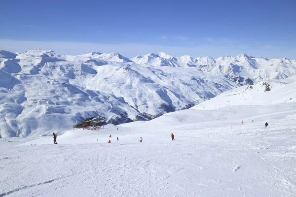 Skiers on ski slopes in high Alps resort, apres ski chalet, with snowy mountain peaks