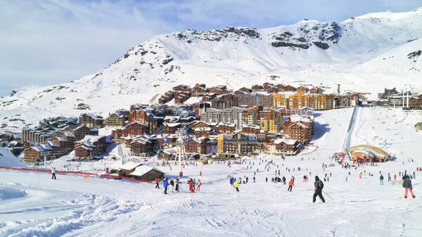 Skiers and snowboarders on a wide slope going to Val Thorens French village, the highest ski resort in Europe. Snowy Alps peaks with downhill pistes surround the alpine village.