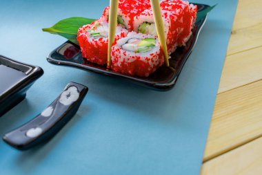 Çubuklu bir tabakta tobiko havyarlı suşi, mavi arka plan.