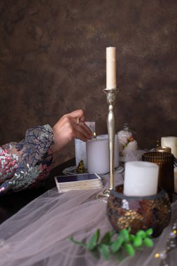 Kadın elinde bir tarot kartı tutuyor. Tarot kartlarında falcılık, sihirli ayinler için mumlar. Gizemli.