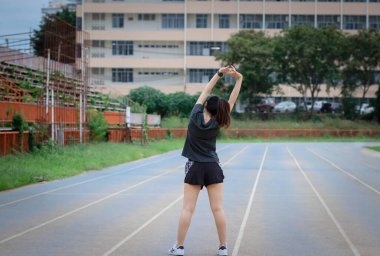 Genç bir kadın parkta dışarıda antrenman yapıyor. O, kollarını uzatıyor ve başka yere bakıyor. Sağlık hizmetleri,