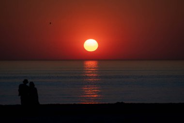 Kuzey Hollanda sahillerinde gün batımını izleyen bir çiftin silueti.