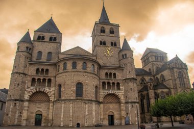 Trier, Almanya 'daki Aziz Peter Katedrali' nin Roma cephesi çarpıcı kuleleri ve tarihi taş duvarları dramatik, altın bir gökyüzünün altında..