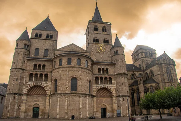 Trier, Almanya 'daki Aziz Peter Katedrali' nin Roma cephesi çarpıcı kuleleri ve tarihi taş duvarları dramatik, altın bir gökyüzünün altında..