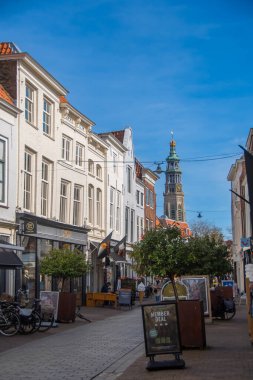 Middeburg, Hollanda, 21 Mart 2025, tarihi Middelburg kasabasında büyüleyici yaya bölgesi, açık mavi gökyüzü altında çarpıcı bir kilise kulesi manzarası var..