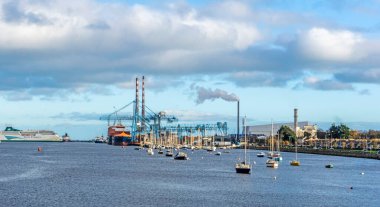 A view of Dublin Port, Ireland, with a gantry crane in operation, a passenger ferry berthed,  small boats and the East Link Ferry Bridge and the new incinerator in the distance.  clipart