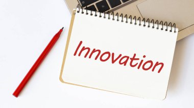 Dizüstü bilgisayar, kırmızı kalem ve beyaz arka planda metin INNOVATION ile not defteri