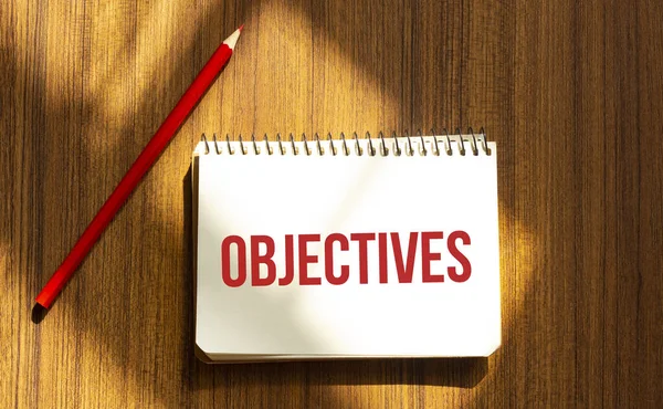 Beyaz arkaplanda OBJECTIVES yazılı kırmızı kalem ve not defteri