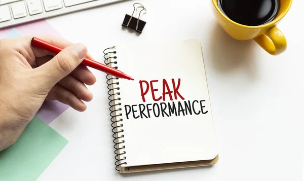 Kırmızı kalemle. Kahve fincanı. Kal. Klavye ve beyaz arka plan. Not defterinde Peak Performans İşareti