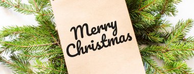 Kahverengi not defteri bir noel ağacının dallarında yatıyor. Mutlu Noeller yazılı.