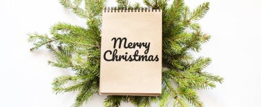Kahverengi not defteri bir noel ağacının dallarında yatıyor. Mutlu Noeller yazılı.