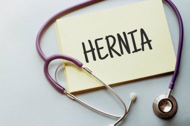 Mor arkaplanda sarı listeli steteskop ve HerNIA metni.