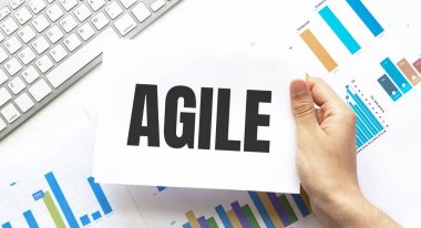 İş adamı elinde AGILE yazılı bir kart tutuyor. Klavye, diyagram ve beyaz arkaplan