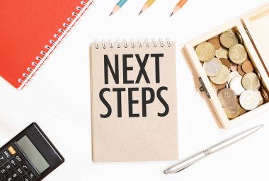 Hesap makinesi, kırmızı not defteri, üç renkli kalem, gümüş kalem ve NEXT STEPS yazılı kahverengi defter.