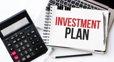 Dizüstü bilgisayar, hesap makinesi, kalem ve not defteri beyaz arkaplan üzerinde INVESTMENT PLAN