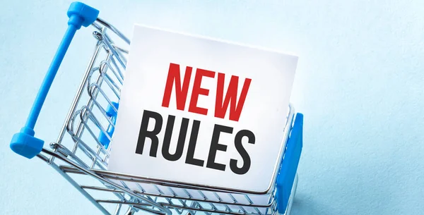Shopping cart and text new rules on white paper note list. Shopping list concept on blue background.