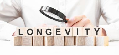 İş adamı elinde büyüteç tutuyor. İşadamı, tahta küplere LONGEVITY yazısıyla bakıyor. Finansal. finansman