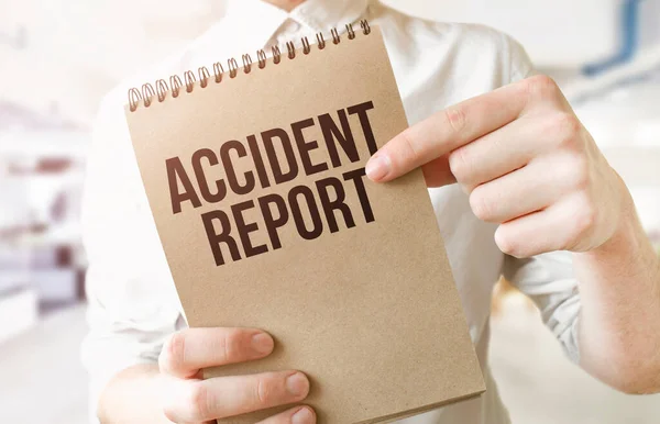 Text Accident Report on brown paper notepad in businessman hands in office. Business concept