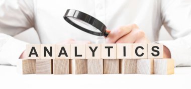 İş adamı elinde büyüteç tutuyor. İş adamı, tahta küplere ANALYTICS yazısıyla bakıyor. Finansal. finansman