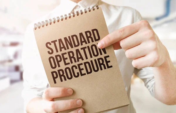 Text Standard Operation Procedure on brown paper notepad in businessman hands in office. Business concept