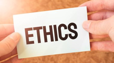 Bir iş adamının elindeki beyaz kart kâğıdına ETHICS kelimesi kazınmış. Özet konsepti. kırmızı ve beyaz kağıt