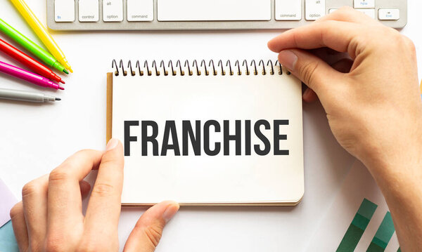 Бизнесмен держит блокнот с текстом FRANCHISE. Белый фон. Бизнес