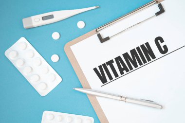 İçinde hap, kalem, tıbbi konsept ve üst görünüm olan bir masanın üzerinde VITAMIN C metni olan defter sayfası.