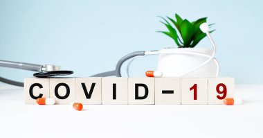 COVID 19 kelimesi ahşap bir arka planda steteskopun yanındaki tahta küplere yazılmıştır. Tıbbi konsept