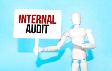 Tahta adam elinde InterNAL AUDIT yazan beyaz bir tabela tutuyor. Harflerin içeriğinin iş konsepti ve pazarlama üzerinde etkileri vardır..