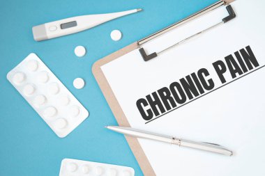Notebook page with text CHRONIC PAIN on a table with a pills and pencil, medical concept, top view