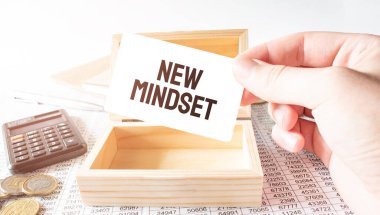Businessman hold white card with text NEW MINDSET Calculator,wood box,money and financial documents