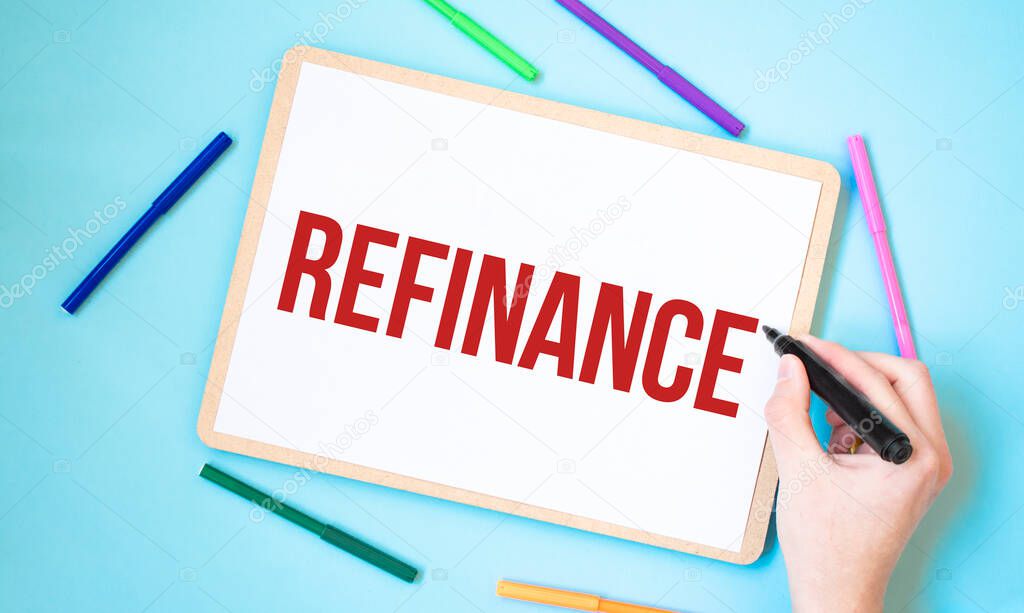 Text REFINANCE on a notebook surrounded by colored felt-tip pens, business concept idea,