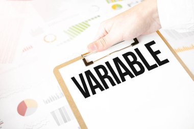 Text VARIABLE on white paper plate in businessman hands with financial diagram. Business concept