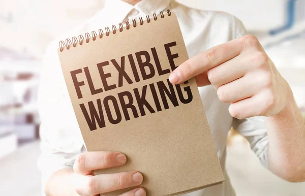 Text FLEXIBLE WORKING on brown paper notepad in businessman hands in office. Business concept