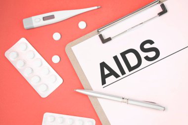İçinde hap, kalem, tıbbi konsept ve üst görünüm olan bir masada AIDS mesajı olan defter sayfası.