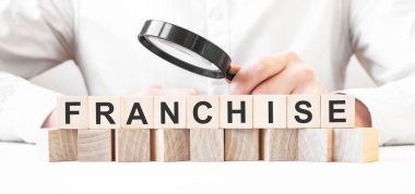 İş adamı elinde büyüteç tutuyor. İşadamı ahşap küplere FRANCHISE yazısıyla bakıyor. Finansal. finansman