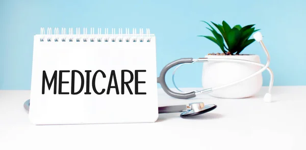 The text MEDICARE is written on notepad near a stethoscope on a blue background. Medical concept