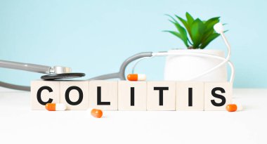 COLITIS kelimesi ahşap bir arka planda steteskopun yanındaki tahta küplere yazılmıştır. Tıbbi konsept