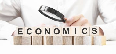İş adamı elinde büyüteç tutuyor. İş adamı ECONOMICS yazılı tahta küpleri izliyor. Finansal. finansman