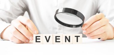 Elinde büyüteç ve tahta blok tutan bir iş adamı. İş adamı, tahta küpleri yazılı bir etkinlikle izliyor. Finansal. finansman