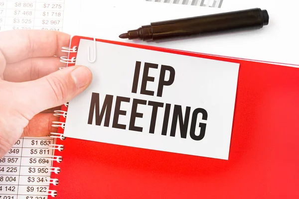 İş adamı elinde kırmızı defter ve IEP buluşması yazılı beyaz kart tutuyor. Mali konsept