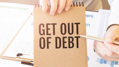 Yazı, kahverengi kâğıt not defterine yazılan borçtan kurtulmak için iş adamlarının elinde diyagramla masanın üzerinde duruyor. İş konsepti